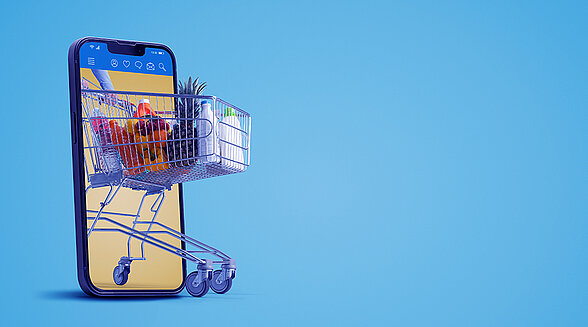 Smartphone mit einem beladenen Einkaufswagen, der aus dem Handybildschirm herausfährt